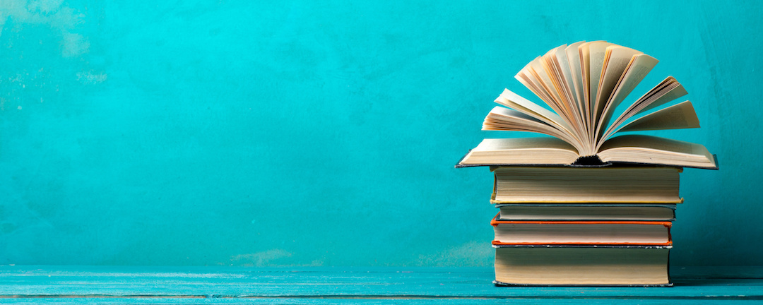 A pile of hardback books against a turquoise background.
